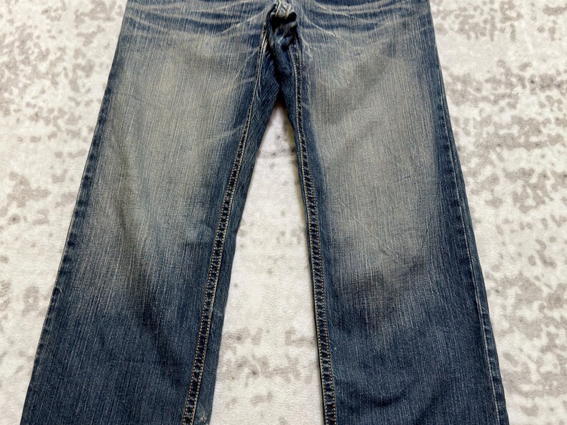May include: Faded blue denim jeans with a classic five-pocket design. The jeans have a straight leg cut and feature visible stitching along the seams and pockets. The denim has a worn, distressed appearance.