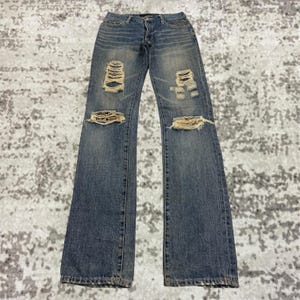 Könnte beinhalten: Blaue Jeans aus Denim mit Distressed-Details, mit zerrissenen Bereichen an Knien und Oberschenkeln. Die Jeans haben ein klassisches Fünf-Taschen-Design und eine verblasste Waschung. Die Jeans liegen flach auf einer gemusterten Oberfläche.