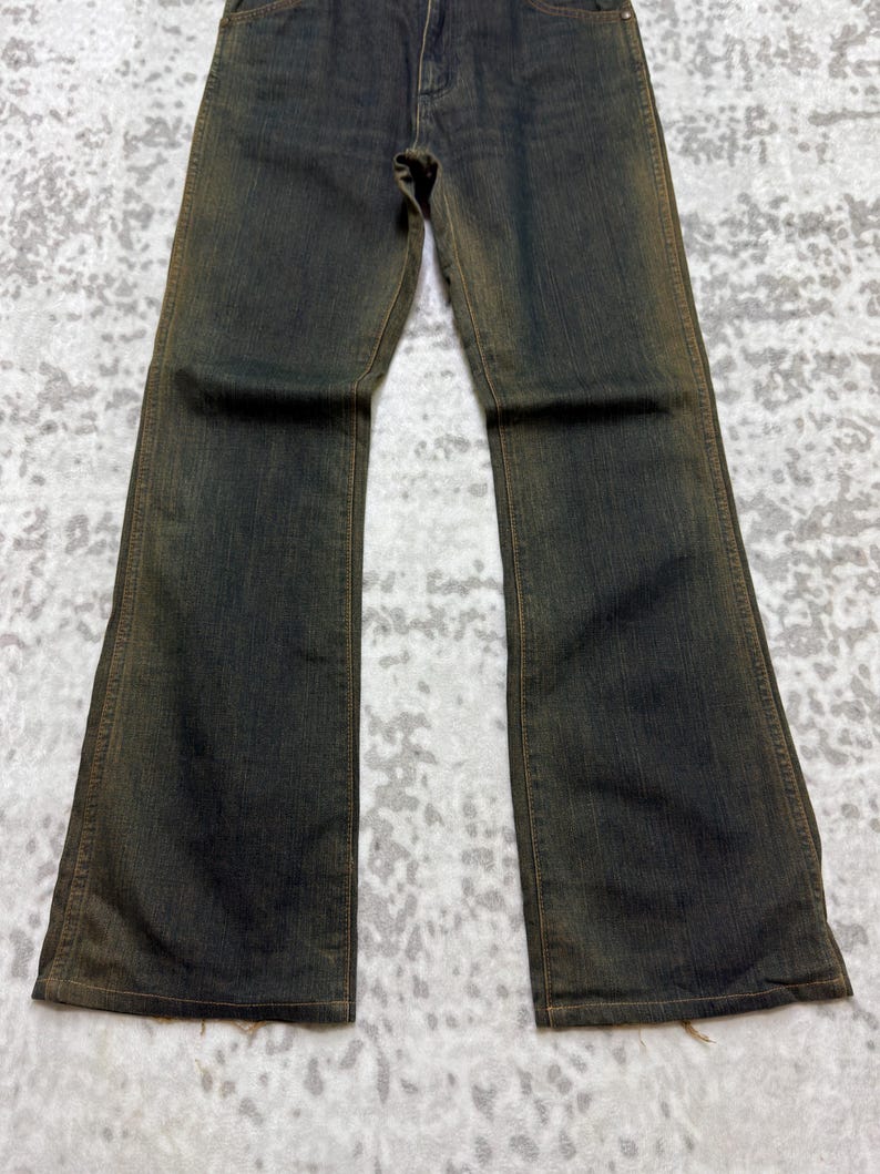 May include: Dark wash denim jeans with a slight flare at the bottom. The jeans have a faded, worn appearance with subtle color variations. The fabric appears to be a medium weight, suitable for everyday wear.