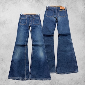 Könnte beinhalten: Zwei Paar Vintage-Jeans aus blauem Denim mit Schlaghose. Die Jeans haben ein klassisches Fünf-Taschen-Design mit zwei Vordertaschen und zwei Gesäßtaschen. Die Jeans hängen an Holzbügeln vor einem neutralen Hintergrund.