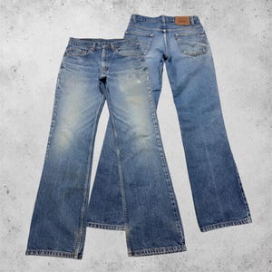 Könnte beinhalten: Zwei Paar blaue Jeans aus Denim. Ein Paar ist von vorne mit Knopfleiste und verwaschener Optik zu sehen. Das zweite Paar ist von hinten abgebildet und zeigt zwei Gesäßtaschen mit Ziernähten, einen braunen Lederaufnäher und ein rotes Etikett.