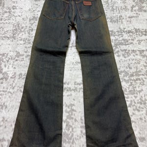 May include: Vintage denim jeans with a flared leg design. The jeans are a dark wash with a faded, worn appearance. Features include classic five-pocket styling, a brown leather patch, and a metal zipper. The jeans are displayed on a hanger.