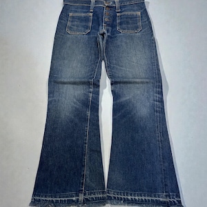 May include: Blue denim jeans with a button fly and two front pockets. The jeans have a flared leg and a raw hem. The denim has a faded appearance, with lighter areas on the thighs and knees.