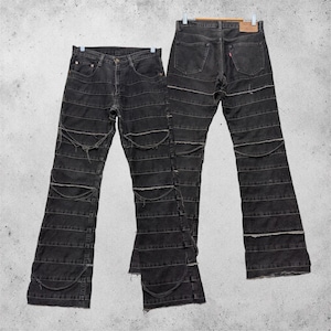 Könnte beinhalten: Eine schwarze Jeans aus Denim mit horizontaler Paneelkonstruktion und ausgefransten Kanten entlang der Nähte. Die Jeans verfügt über ein klassisches Fünf-Taschen-Design, einen Knopfverschluss und einen beigen Lederaufnäher am Bund.