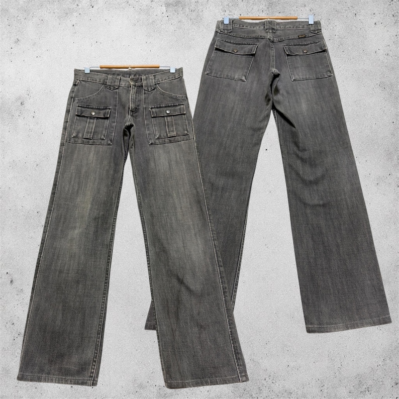 May include: Two pairs of gray denim jeans are displayed, hanging on wooden hangers. The jeans have a classic five-pocket design, with two cargo pockets on the front and two on the back. The denim has a faded, worn look.