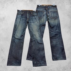 Könnte beinhalten: Zwei Paar dunkelblaue Jeans aus Denim mit verwaschener Optik. Ein Paar ist von vorne abgebildet und zeigt einen Knopfverschluss sowie fünf Taschen, während das andere Paar von hinten zu sehen ist und zwei Gesäßtaschen aufweist.
