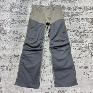 May include: Two-tone work trousers in olive green and grey. The trousers have a classic five-pocket design with a button and zip closure. The legs are wide and feature reinforced panels at the knees.
