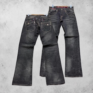 Könnte beinhalten: Eine dunkelgraue Jeans aus Denim mit verwaschener Optik, Sitzfalten-Details und Bootcut-Schnitt. Die Gesäßtaschen haben silberfarbene Knopfverschlüsse und Stickereien, während die Vorderseite einen klassischen Knopfverschluss aufweist.