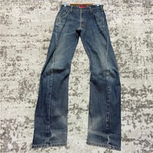 May include: Blue denim jeans with a faded wash and white stitching details. The jeans have a classic five-pocket design and a straight leg fit. The jeans are hanging on a wooden hanger.