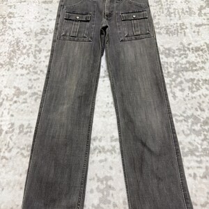 May include: A pair of gray denim pants with two front pockets and a button and zipper closure. The pants are hanging on a hanger against a light-colored background. The pants have a straight leg design.