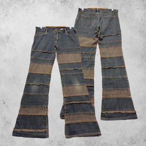 Könnte beinhalten: Zwei Paar blaue Jeans aus Denim mit horizontalem Patchwork-Design aus abwechselnden dunkelblauen Denim- und braunen Stoffbahnen. Die Jeans haben einen ausgestellten Beinschnitt mit sichtbaren ausgefransten Kanten an jeder Naht und einen Knopfverschluss.