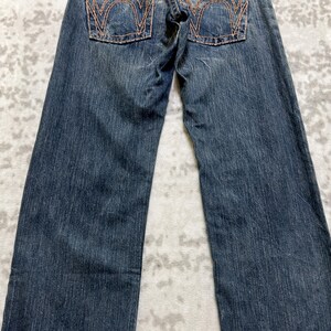 May include: Dark blue denim jeans with orange stitching details on the back pockets. The jeans have a classic five-pocket design and a straight leg cut. The denim has a slightly faded appearance.