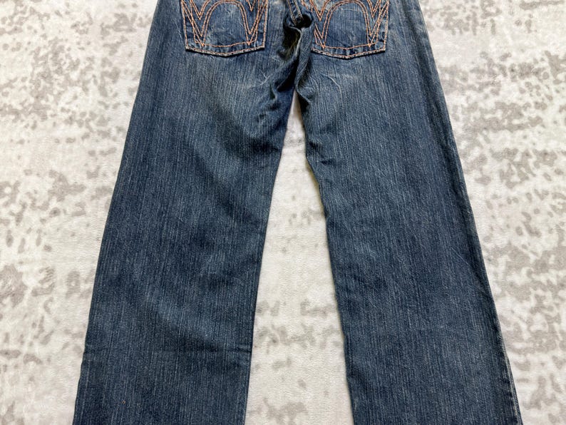 May include: Dark blue denim jeans with orange stitching details on the back pockets. The jeans have a classic five-pocket design and a straight leg cut. The denim has a slightly faded appearance.