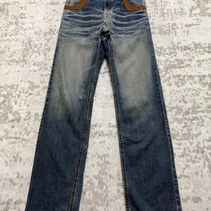 May include: Blue denim jeans with a faded wash and brown suede pocket accents. The jeans have a classic five-pocket design and a straight leg fit. The jeans are hanging on a wooden hanger.