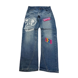 Könnte beinhalten: Hellblaue Jeans mit dekorativen Aufnähern. Einer zeigt Minnie Mouse mit dem Text "Minnie Mouse". Ein weiterer Aufnäher zeigt die Zahl "1928". Die Jeans haben ein weites Bein-Design.