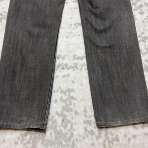 May include: Close-up of gray denim jeans. The jeans are a solid, medium gray color with a slightly faded appearance. The legs are straight cut, and the fabric has a subtle texture. The jeans are laid flat, showcasing the front of the garment.