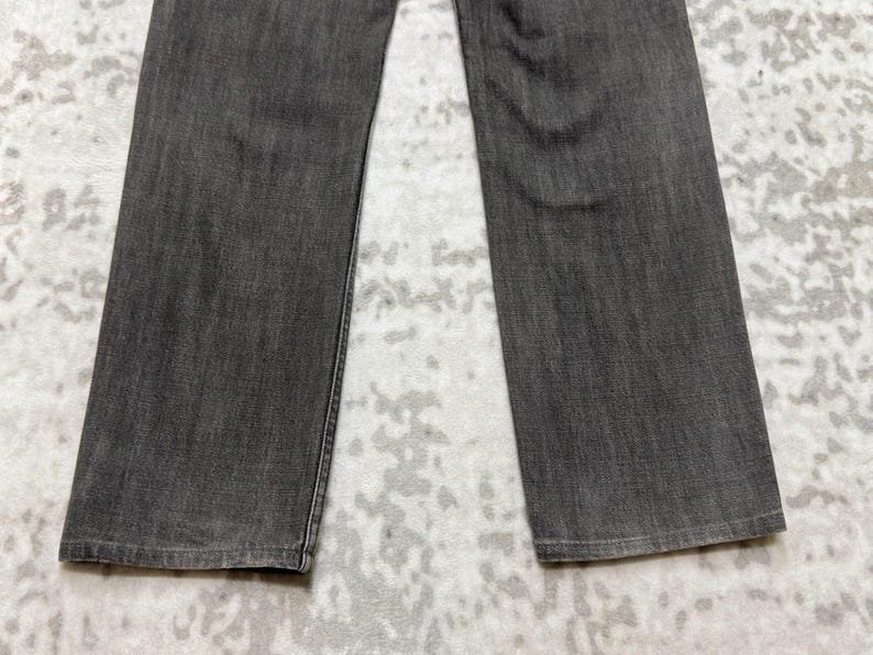 May include: Close-up of gray denim jeans. The jeans are a solid, medium gray color with a slightly faded appearance. The legs are straight cut, and the fabric has a subtle texture. The jeans are laid flat, showcasing the front of the garment.