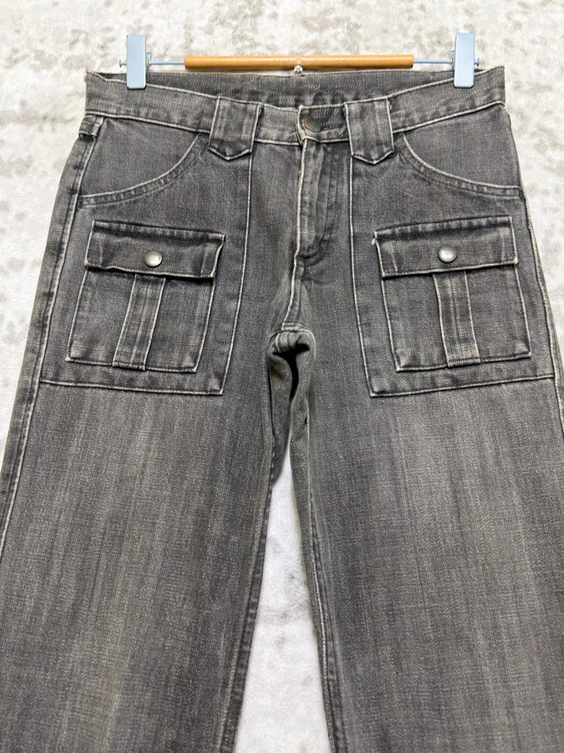 May include: Close-up of gray denim pants with two front pockets and two side pockets. The pants have a button and zipper closure and belt loops. The denim has a faded appearance.