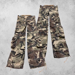 Könnte beinhalten: Zwei Cargohosen mit Camouflage-Muster in Braun-, Olivgrün- und Beigetönen. Jede Hose verfügt über mehrere aufgesetzte Taschen mit Klappen und Knopfverschlüssen sowie verstellbare Kordelzüge an den Beinabschlüssen für eine individuelle Passform.