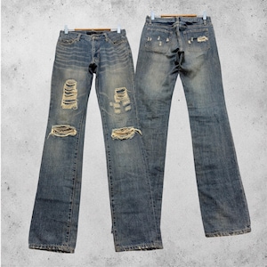 Könnte beinhalten: Blaue Jeans aus Denim mit Distressed-Details, einschließlich zerrissener Knie und Patches. Die Jeans werden von vorne und hinten gezeigt, wobei die ausgewaschene Optik und das Design hervorgehoben werden. Die Jeans hängen an einem Holzbügel.