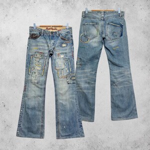 Könnte beinhalten: Hellblaue Jeans aus Denim mit ausgestelltem Bein, abgenutzten Flicken und sichtbaren mehrfarbigen Nähten. Die Vorderseite zeigt verschiedene rechteckige Stoffflicken und ausgefranste Details, während die Rückseite zwei Taschen mit Ziernähten aufweist.