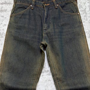 May include: Dark wash denim jeans with a faded, worn appearance. The jeans have a classic five-pocket design, a button and zipper closure, and belt loops. The denim has a slight sheen, and the jeans are hanging on a hanger.