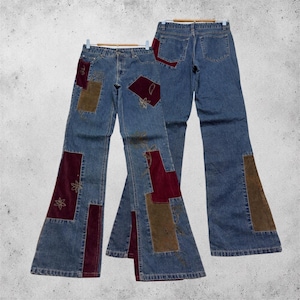 May include: Two pairs of blue denim jeans featuring flared legs and patchwork accents. The patches consist of rectangular and irregular shapes in burgundy and olive green velvet fabric, with embroidered floral details on the denim surface.