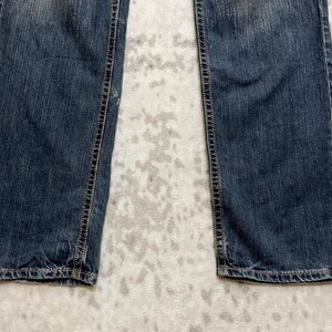 May include: Close-up of the lower portion of a pair of blue denim jeans. The jeans have a classic five-pocket design with visible stitching along the seams and a faded wash. The fabric appears worn and soft.