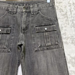 May include: Close-up of gray denim pants with two front pockets and two side pockets. The pants have a button closure and belt loops. The denim is a faded gray color.