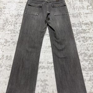May include: Gray denim pants with two square back pockets and a straight leg. The pants are hanging on a wooden hanger. The denim has a slightly faded appearance.