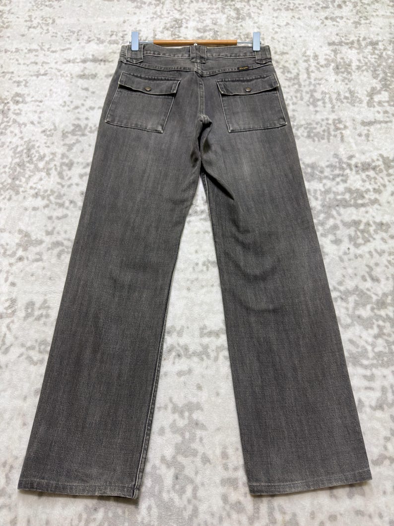 May include: Gray denim pants with two square back pockets and a straight leg. The pants are hanging on a wooden hanger. The denim has a slightly faded appearance.