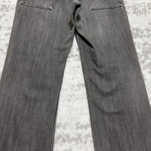 May include: A pair of gray denim jeans. The jeans have a classic five-pocket design with two back pockets. The fabric has a textured appearance, and the jeans appear to be new or in excellent condition.