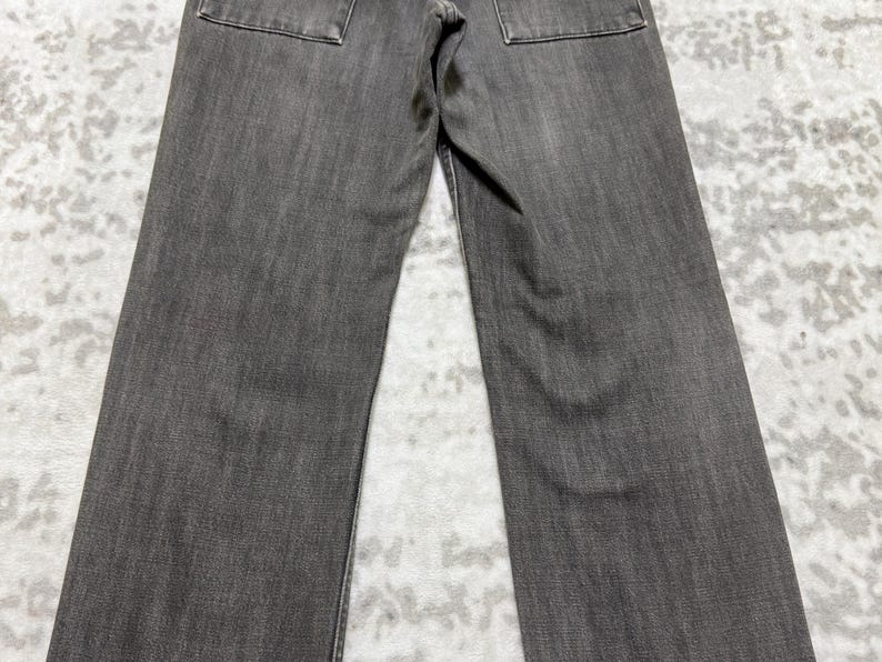 May include: A pair of gray denim jeans. The jeans have a classic five-pocket design with two back pockets. The fabric has a textured appearance, and the jeans appear to be new or in excellent condition.