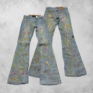 Könnte beinhalten: Zwei Paar hellblaue Schlaghosen aus Denim mit einem lebendigen Farbspritzer-Design in Gelb, Rot und Schwarz. Die Jeans verfügen über eine klassische Fünf-Taschen-Konstruktion, einen Knopf- und Reißverschluss sowie ein ausgestelltes Bein.