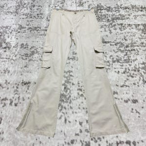 May include: Khaki-colored cargo pants with multiple pockets and a flared leg design. The pants have a button and zipper closure and are made of a durable fabric. The pants are displayed on a hanger.
