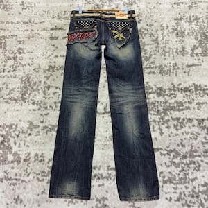 Könnte beinhalten: Dunkelblaue Jeans mit Used-Details. Die Gesäßtaschen haben dekorative Nähte und Verzierungen. Das Wort "pepper" ist rot auf der Gesäßtasche gestickt. Die Jeans hängen an einem Holzkleiderbügel.