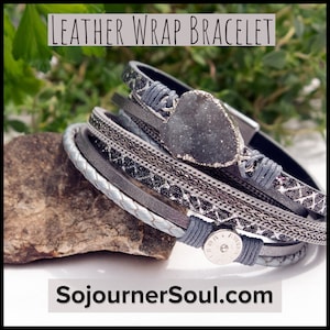 May include: A multi-strand leather wrap bracelet in shades of gray, silver, and black. The bracelet features a large, irregular-shaped gray stone and is accented with braided and patterned bands. The text "LEATHER WRAP BRACELET" and "SojournerSoul.com" are visible.