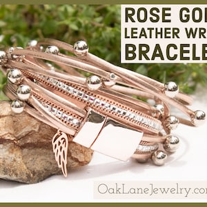 May include: Rose gold leather wrap bracelet with multiple strands, silver-colored beads, and a decorative wing charm. The bracelet features a magnetic clasp and is embellished with clear crystals. The text "Rose Gold Leather Wrap Bracelet" is displayed in the image.