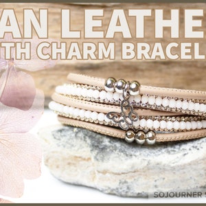 May include: Tan leather wrap bracelet with white beads and a silver butterfly charm. The bracelet is layered with multiple strands of leather and beads.