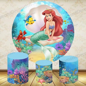 Op de afbeelding: Een kleurrijke achtergrond met Ariel uit De Kleine Zeemeermin, met Botje en Sebastiaan. Drie blauwe cilindrische stands met onderwater scènes maken de feestdecoratieset compleet.