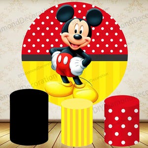 May include: A colorful party backdrop featuring Mickey Mouse. The background is a large red circle with white polka dots, a yellow and black stripe, and a yellow section with vertical stripes. Three cylindrical stands are in the foreground, one black, one yellow with stripes, and one red with white dots.