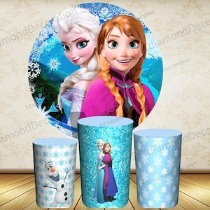 Puede incluir: Tres decoraciones cil&iacute;ndricas para fiestas con personajes de la pel&iacute;cula animada "Frozen". Las decoraciones incluyen im&aacute;genes de Elsa, Anna y Olaf, sobre un fondo de copos de nieve azules y blancos. El tel&oacute;n de fondo presenta a Elsa y Anna.