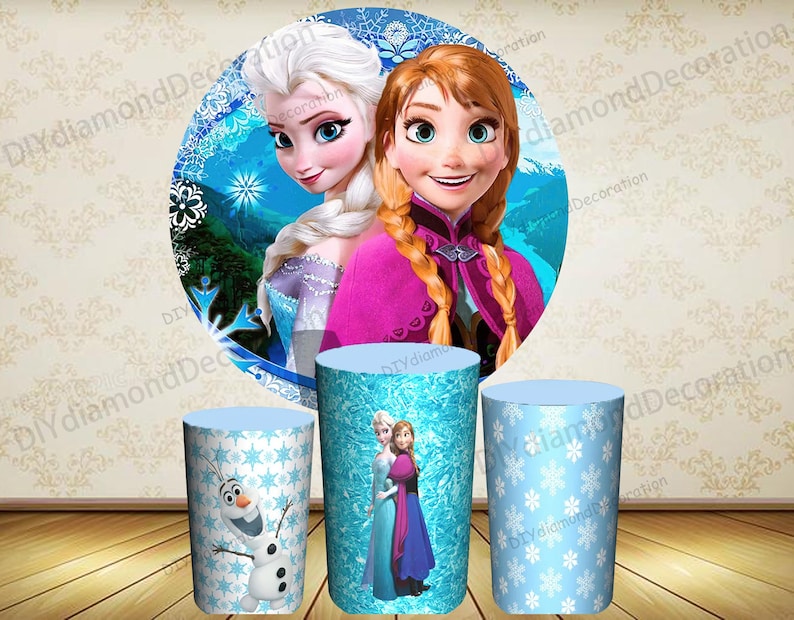 Puede incluir: Tres decoraciones cil&iacute;ndricas para fiestas con personajes de la pel&iacute;cula animada "Frozen". Las decoraciones incluyen im&aacute;genes de Elsa, Anna y Olaf, sobre un fondo de copos de nieve azules y blancos. El tel&oacute;n de fondo presenta a Elsa y Anna.