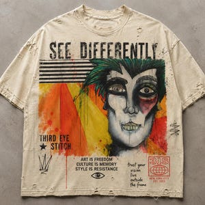 May include: A beige short-sleeve t-shirt with distressed edges featuring a graphic of a stylized face with green hair. Text includes SEE DIFFERENTLY, THIRD EYE STITCH, ART IS FREEDOM CULTURE IS MEMORY STYLE IS RESISTANCE, and 3IS NEW YORK CITY EST. 2023.