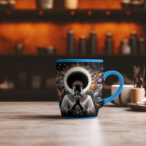 May include: A blue ceramic mug with a black and gold design featuring a woman with her hands clasped in prayer. The woman is surrounded by a galaxy of stars and planets.