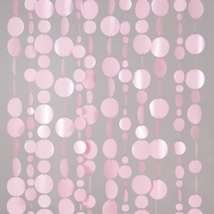 May include: Pink circle garland with multiple strands of varying lengths. The circles are made of shiny, metallic material and are strung together with clear thread.