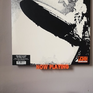 An orange Now Playing display shelf holds the sleeve of Led Zeppelin's first album while the record can be seen playing on the turntable below.
