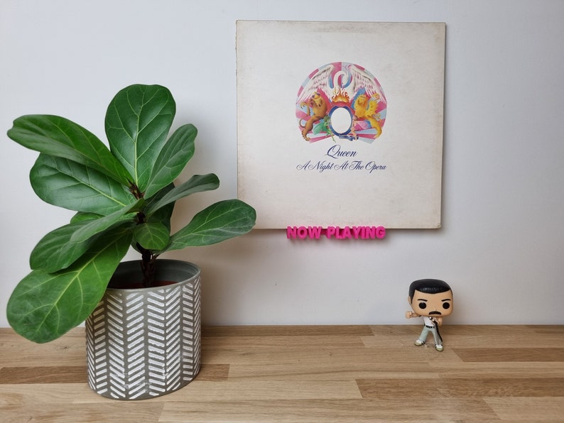 Queen's 'A Night At The Opera' sits on a hot pink Now Playing shelf, while a Funko Pop Freddie Mercury stands in the foreground. There's a plant in the picture, too, for some reason.