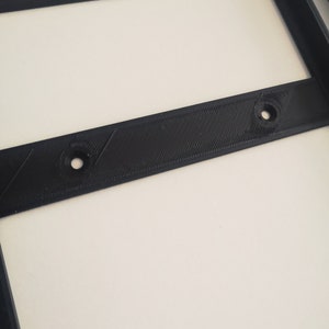 May include: Close-up of a black plastic frame with two small holes. The frame is likely part of a 3D printed object.