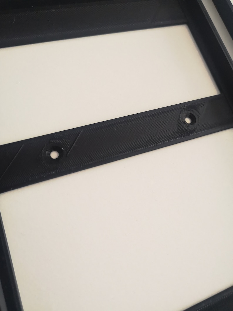 May include: Close-up of a black plastic frame with two small holes. The frame is likely part of a 3D printed object.